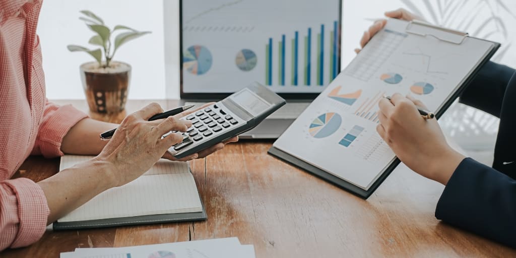 Fotografía de una reunión de trabajo en la que dos personas analizan información financiera. Una sostiene una calculadora y la otra un portapapeles con gráficos estadísticos, mientras al fondo se observa una pantalla con indicadores. La imagen ilustra el análisis y la gestión de información financiera y acompaña la publicación del Decreto 0977 de 2026, relacionado con la reglamentación del derecho a la portabilidad financiera.